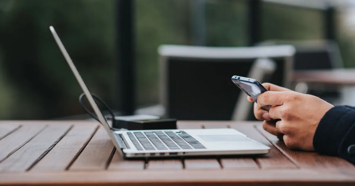 Profissional usando um smartphone ao lado de um notebook em uma mesa de trabalho